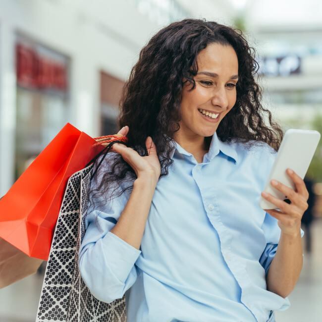 A woman looks at her phone while holding shopping bags.