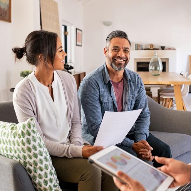 Hispanic couple smiling and sitting opposite a banker