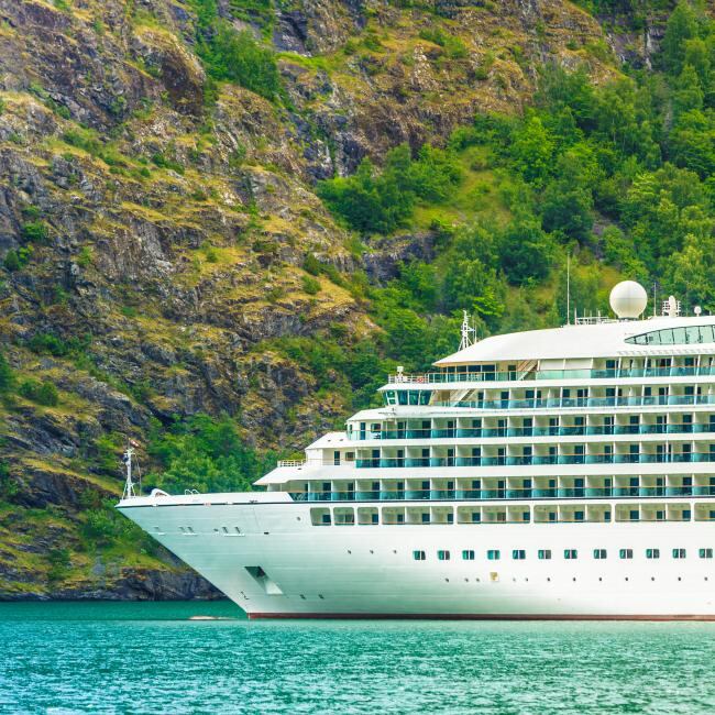 Cruise ship in the water with the backdrop of a mountain covered in green grass.