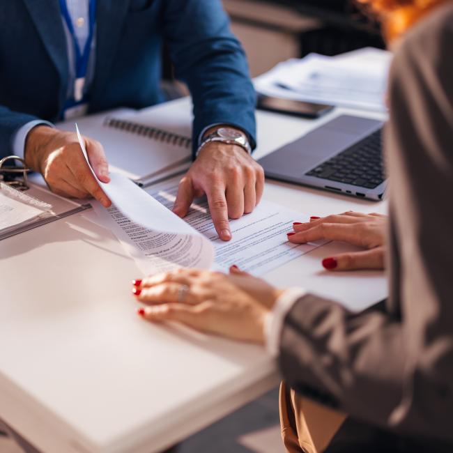A banker and a client sitting opposite each other at a desk reviewing a document. 