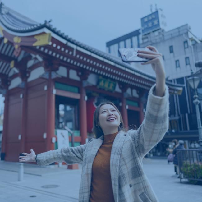 A travel influencer filming a video on her phone in front of a traditional Japanese video. 